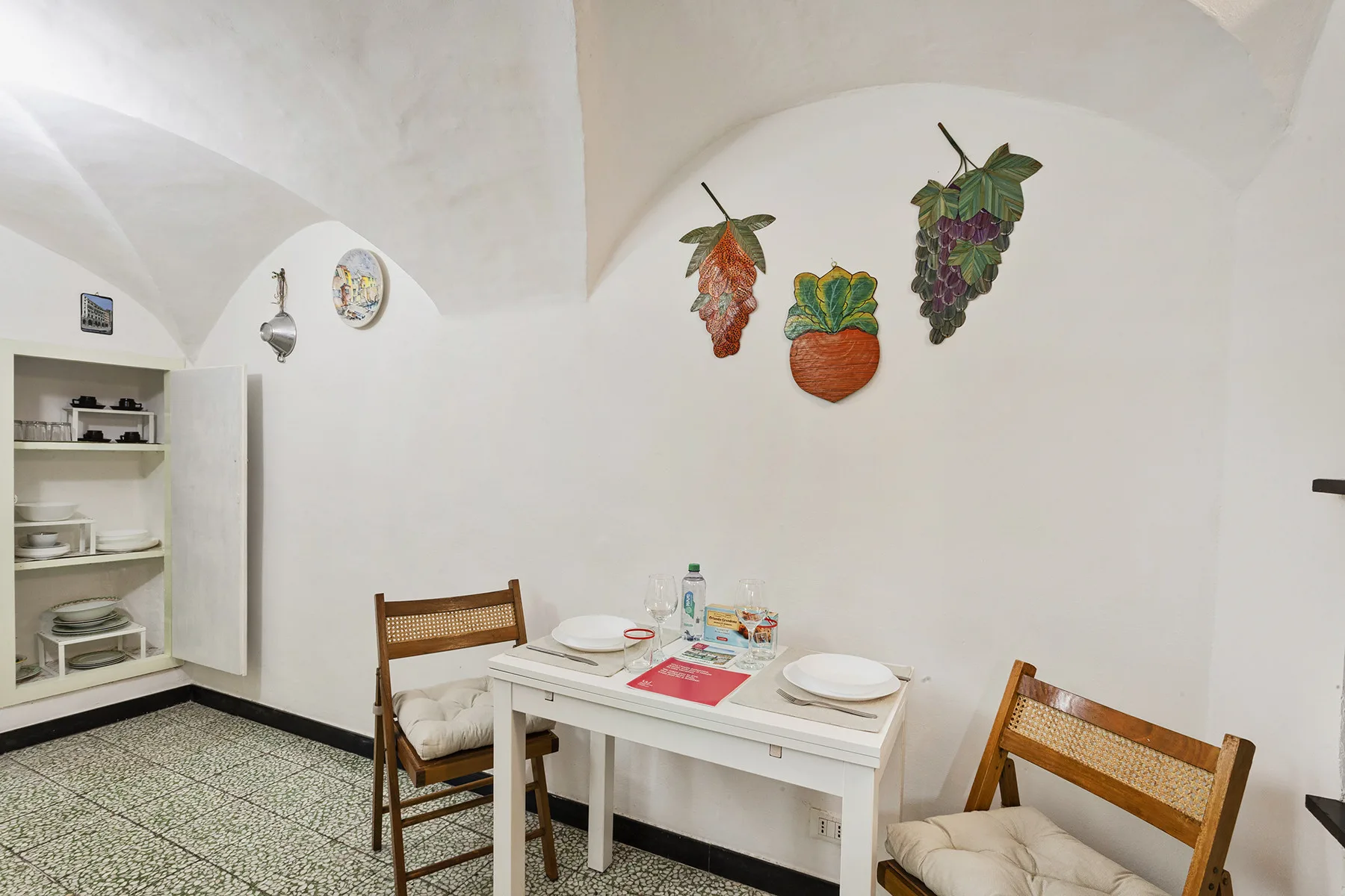 Un comedor con una mesa, asientos y coloridas decoraciones de frutas en la pared.