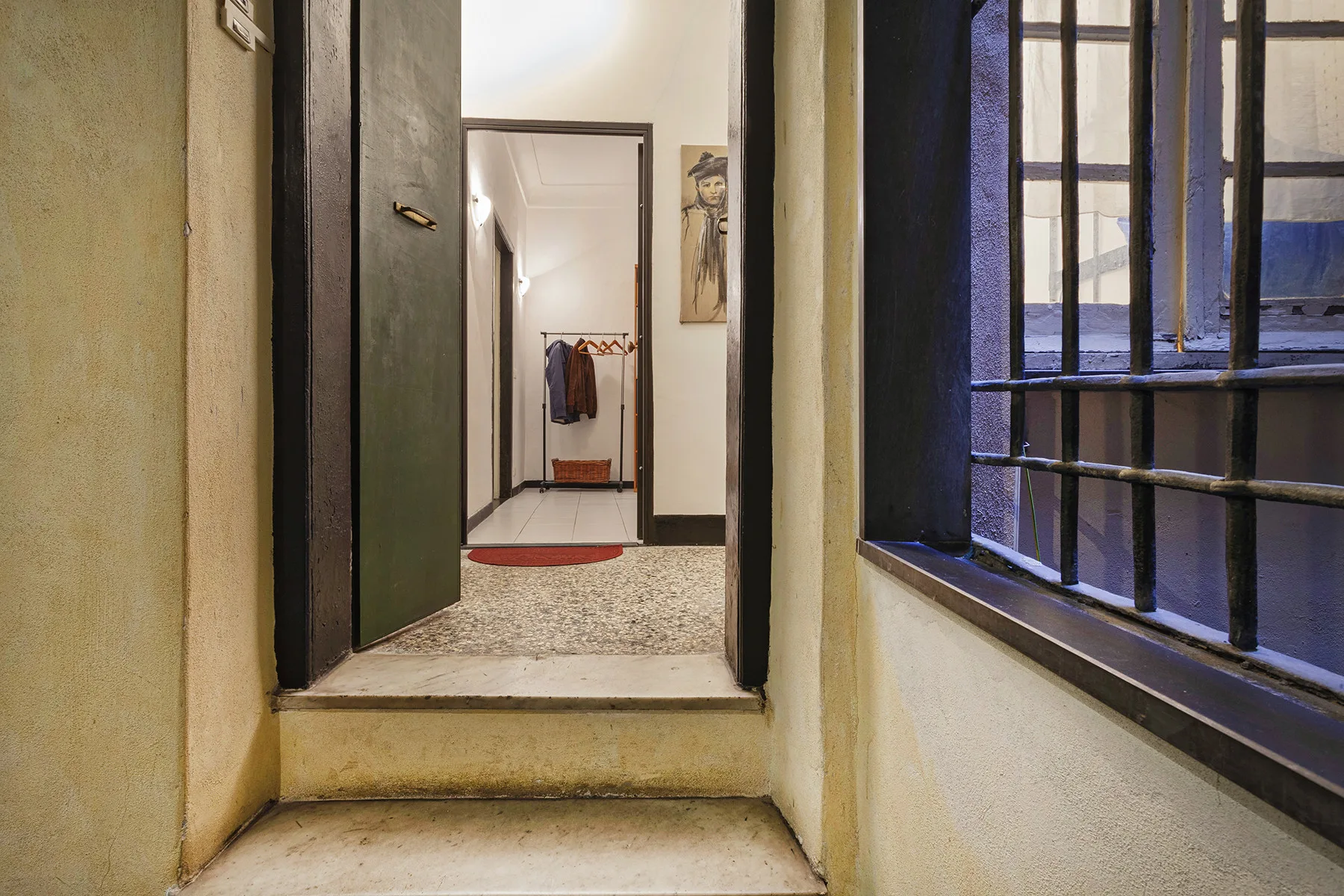 Un pasillo interior da a una habitación con perchero y ventana enrejada.