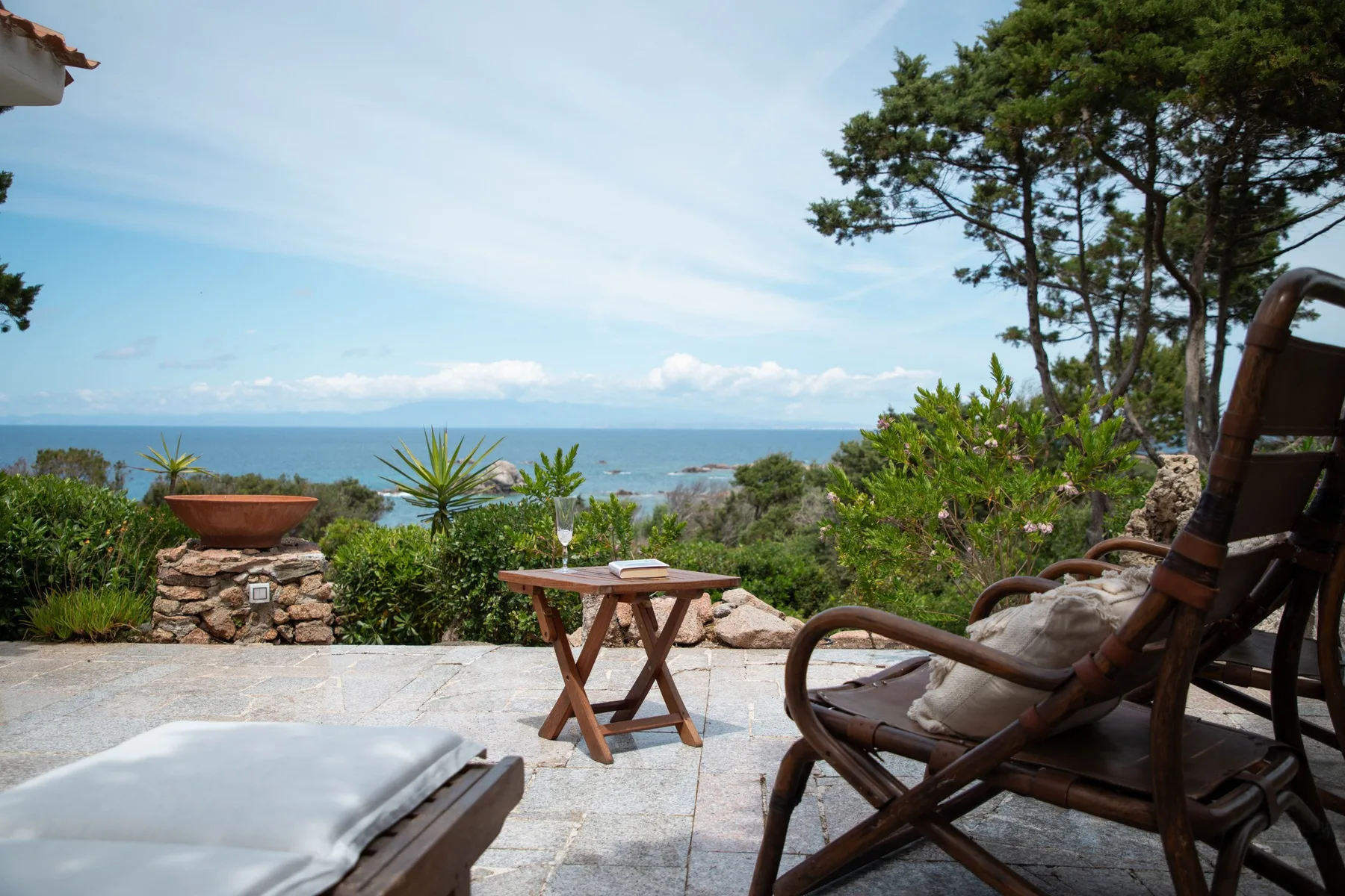 Un patio junto al mar con asientos y una pequeña mesa de madera mira hacia el océano.