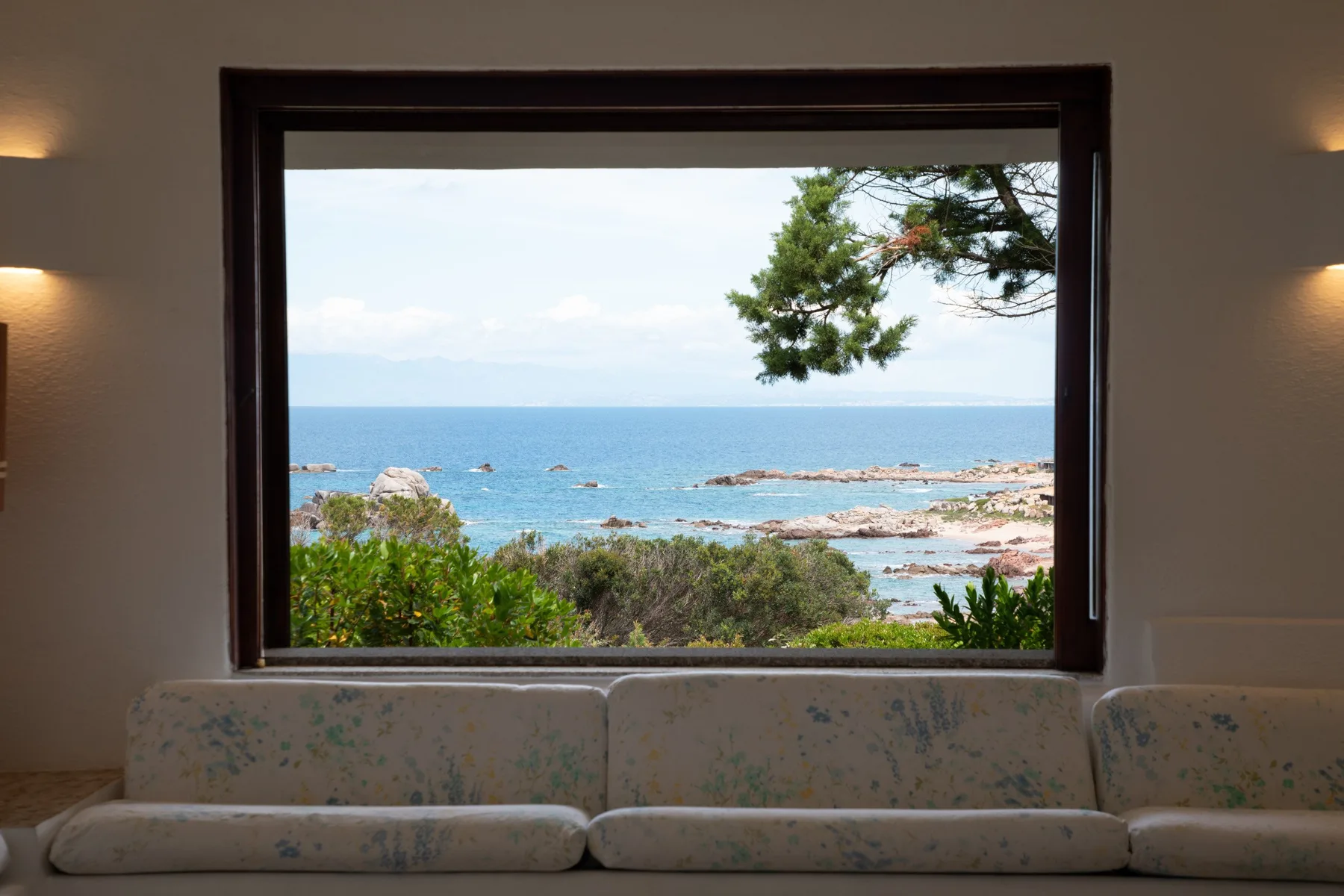 Una zona de estar mira por una gran ventana hacia el mar.