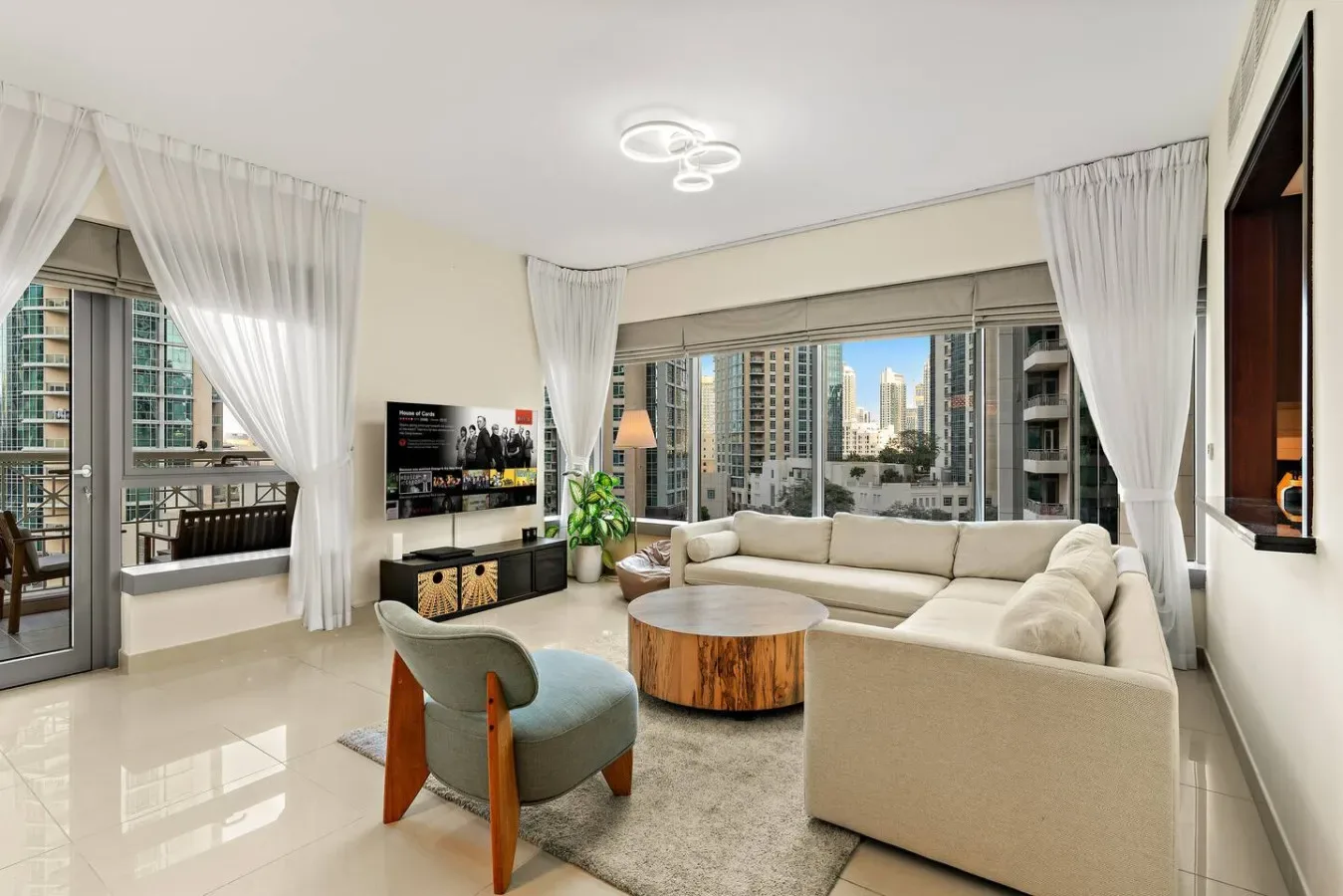 A bright living room with pale seating, a round coffee table, and large windows.