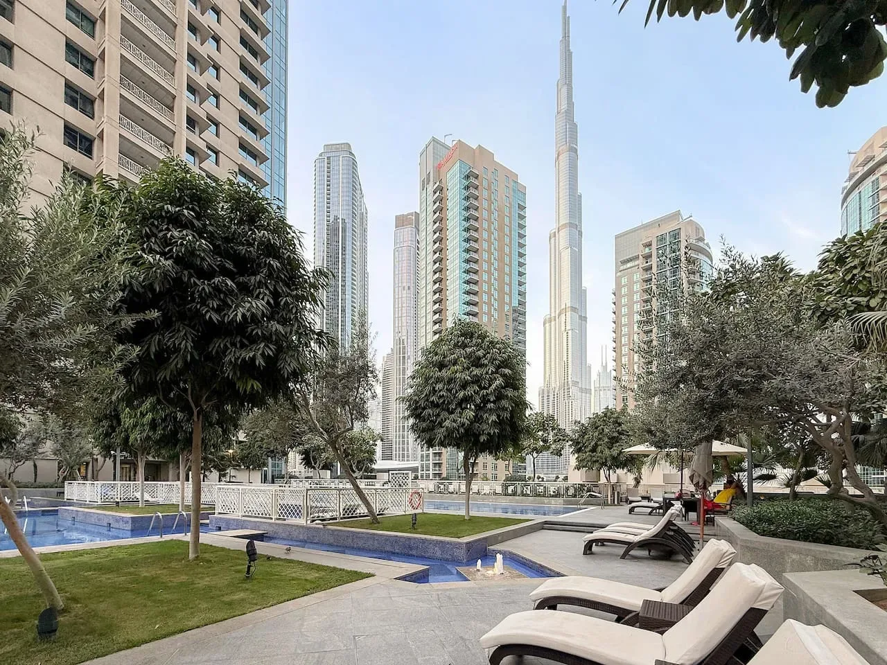 A landscaped outdoor pool area with lounge seating and tall city buildings in the background.