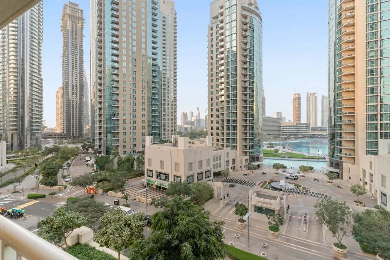 High-rise buildings surround a landscaped urban street and a small waterfront.