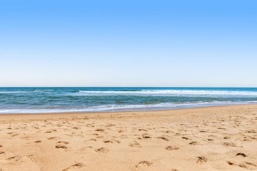 A sandy beach meets gentle ocean waves beneath a clear sky.