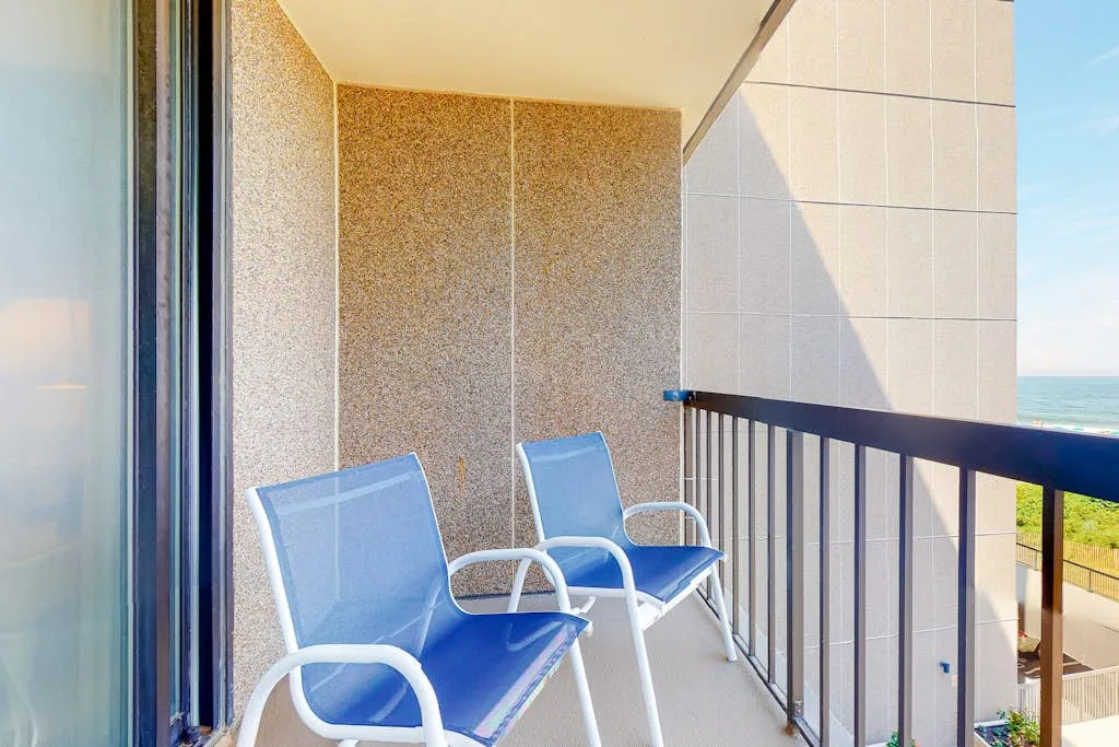 A balcony with blue seating and a railing overlooking the water.