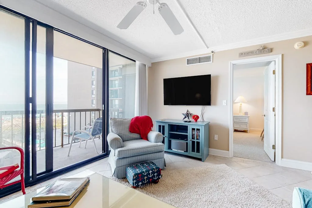 A bright living room with an armchair, television, and sliding glass doors.