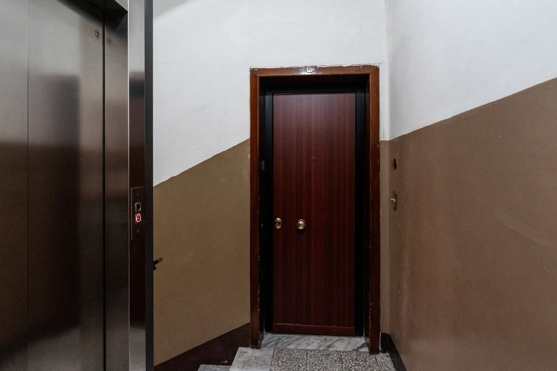 A hallway with an elevator beside a dark wooden door.