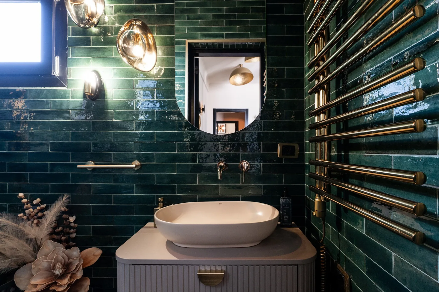 A bathroom with a white basin and dark green tiled walls.