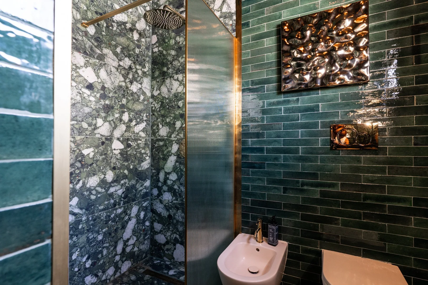 A bathroom with a shower, bidet, and dark green tiled walls.