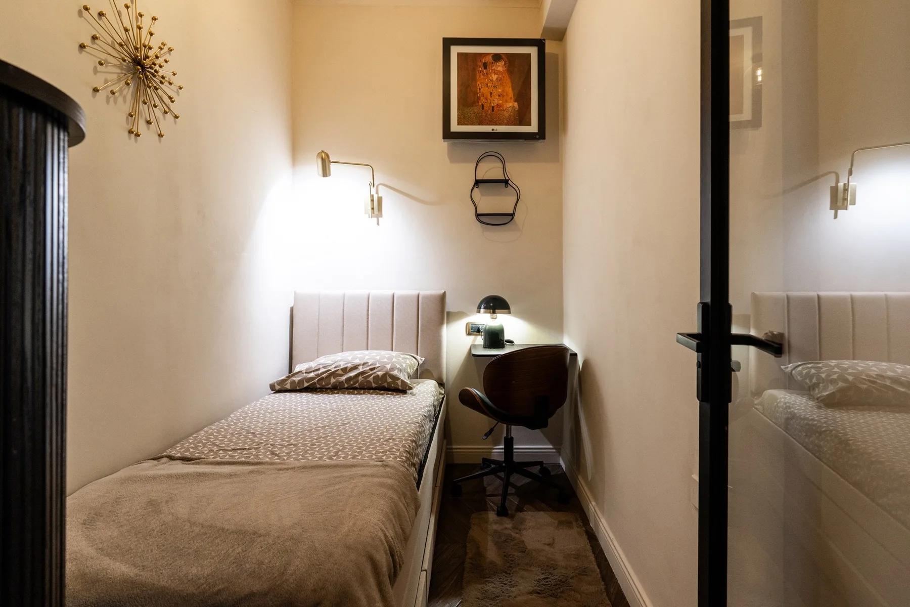 A narrow bedroom with a single bed and a small desk.