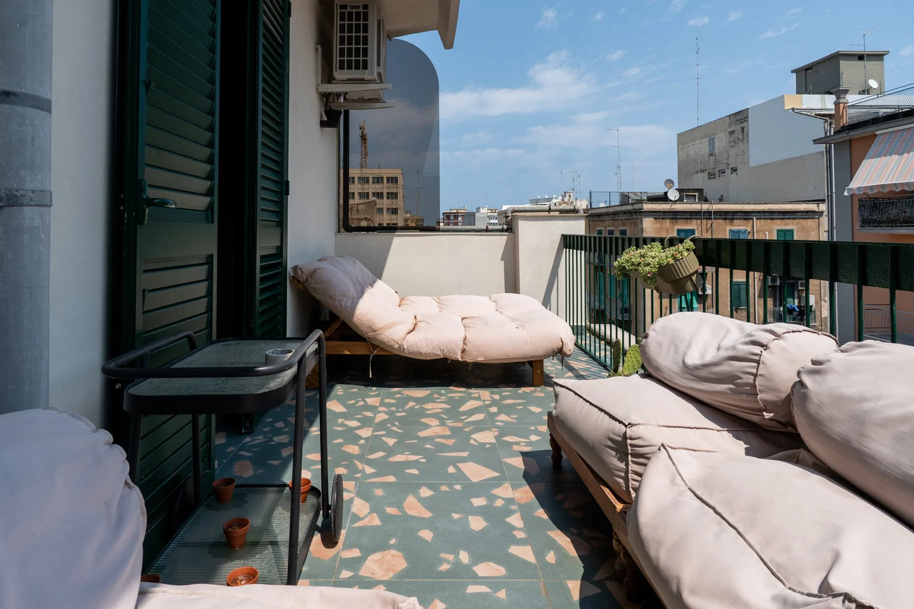A sunny rooftop terrace with cushioned seating and a black metal railing.