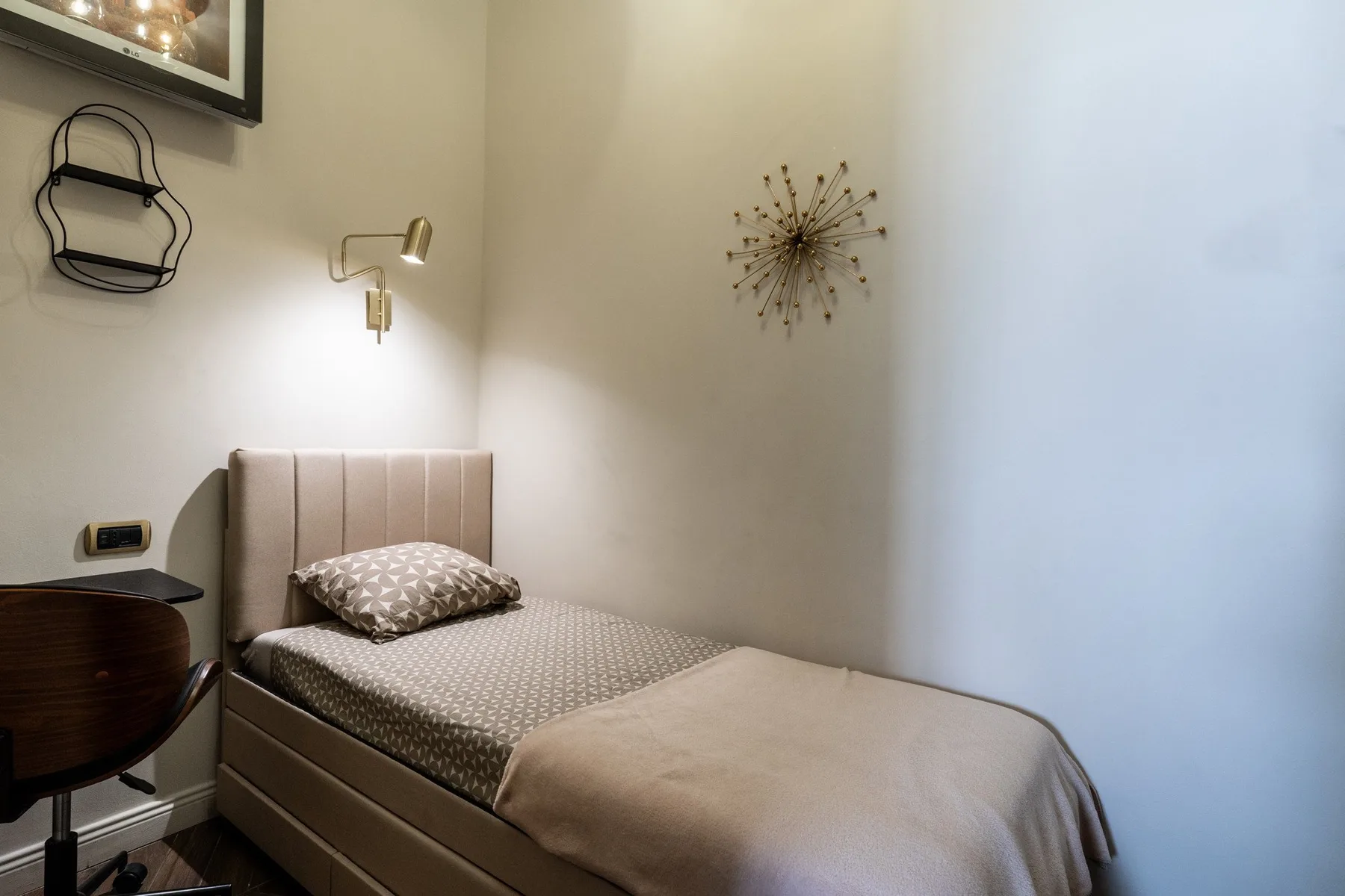 A bedroom with a single bed, patterned bedding, and a wall-mounted light.