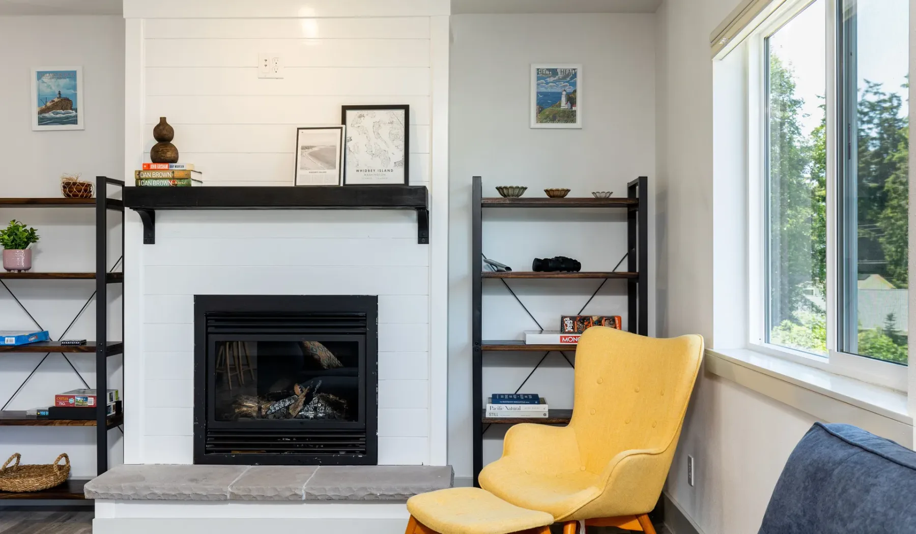 A bright living room with a fireplace, open shelving, and a yellow chair.