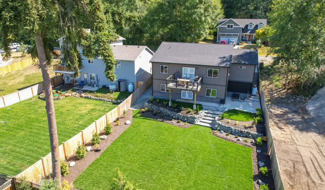 Aerial view of a house with a broad green lawn and surrounding trees.
