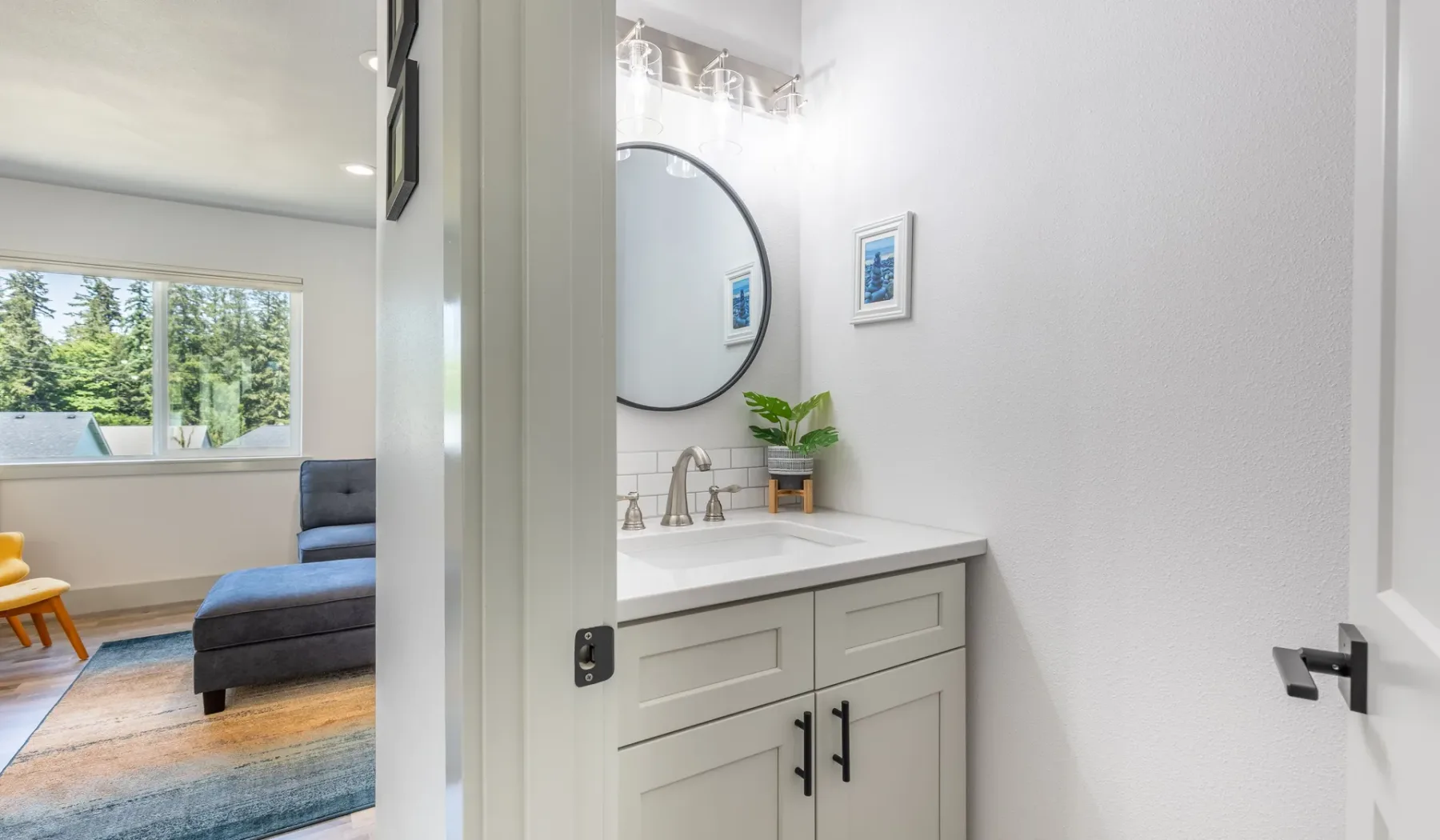 Un tocador de baño con espejo redondo da a una luminosa sala de estar.