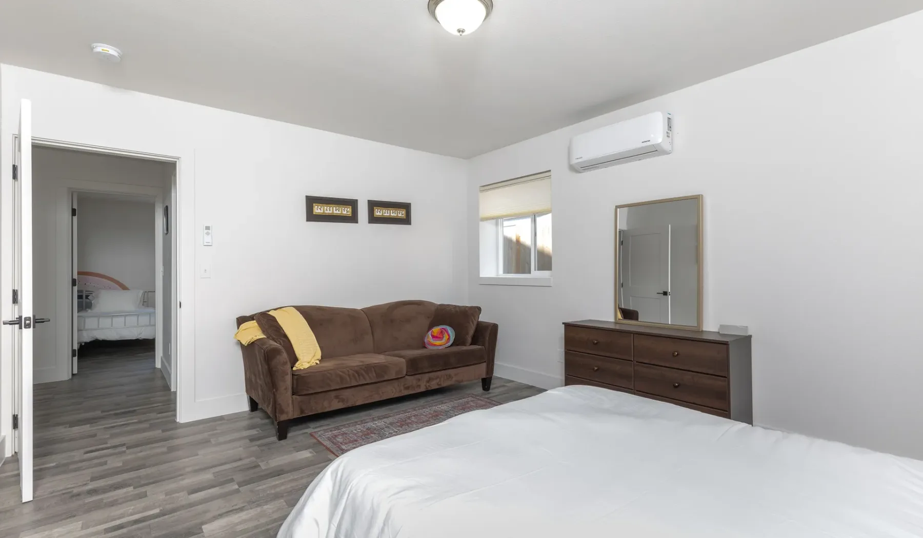 Un dormitorio con una cama, asientos marrones y una cómoda bajo un espejo de pared.