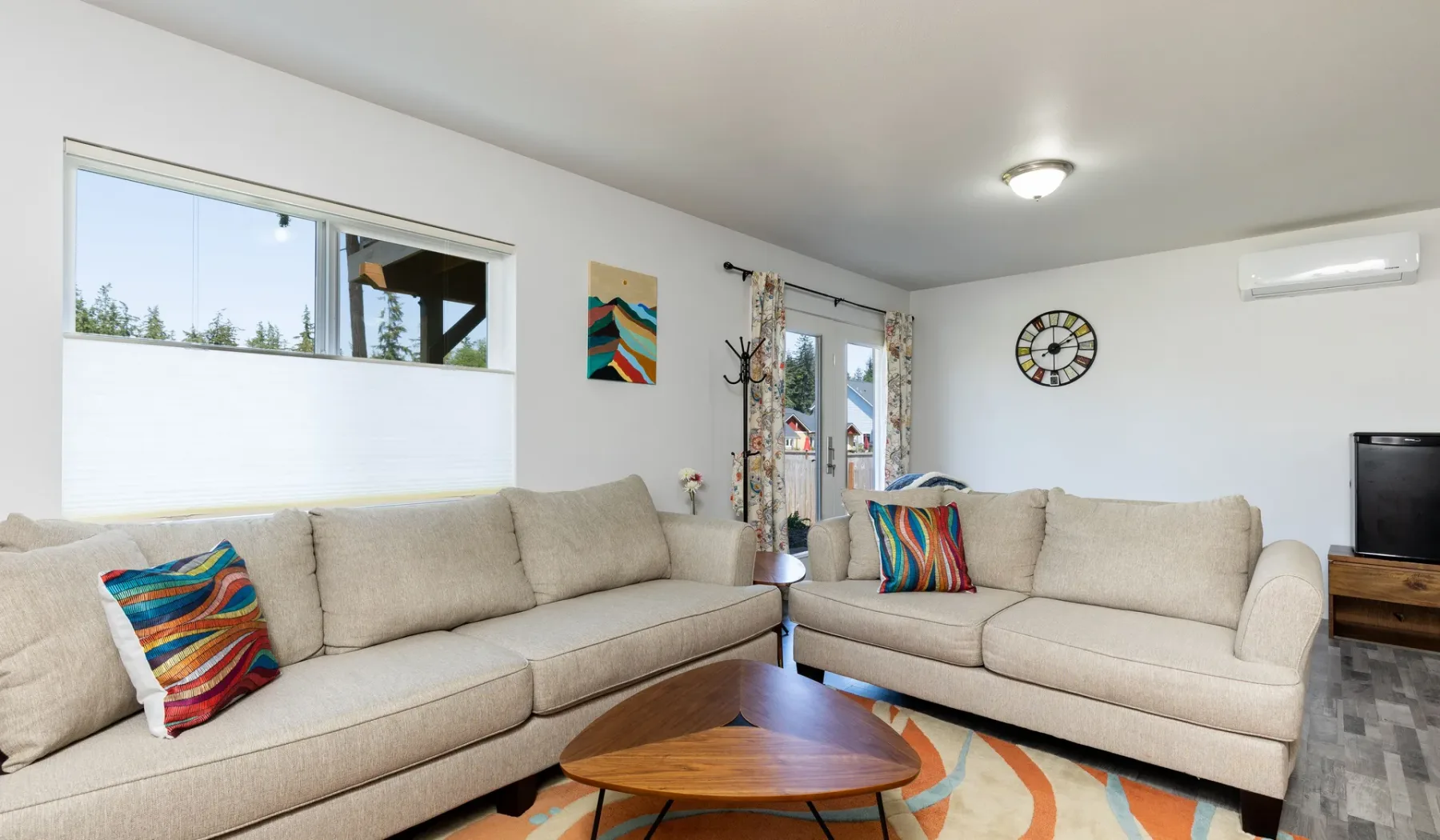 Una sala luminosa con un sofá seccional beige, cojines coloridos y una mesa de centro de madera.