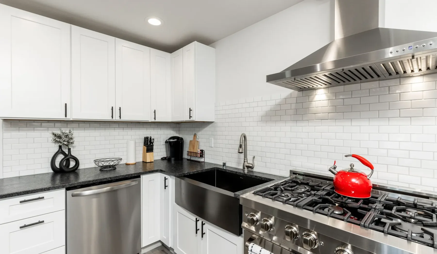 Una cocina luminosa con gabinetes blancos, encimeras oscuras y una estufa de acero inoxidable.