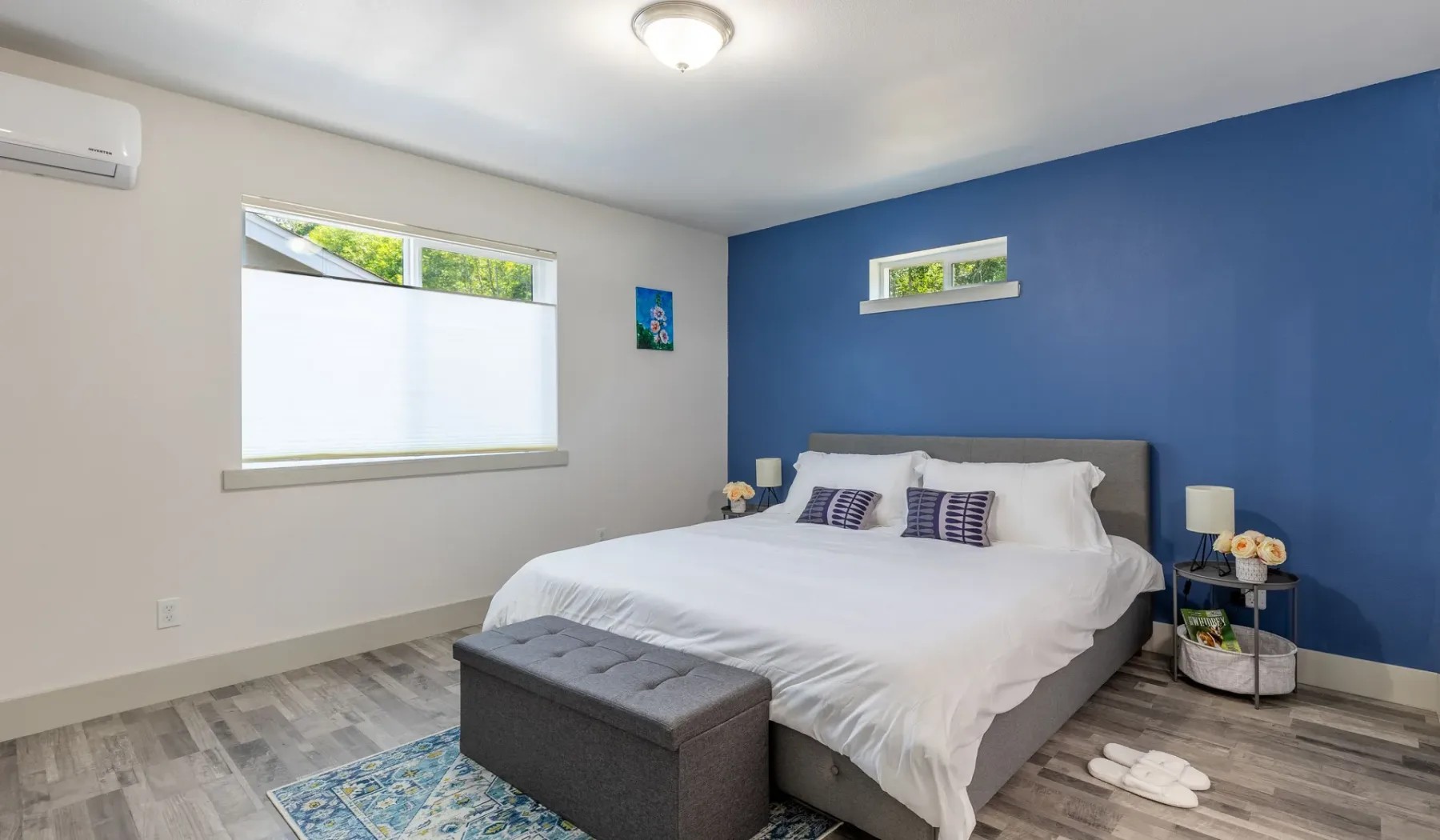 Dormitorio con una cama, un banco gris y una pared azul.