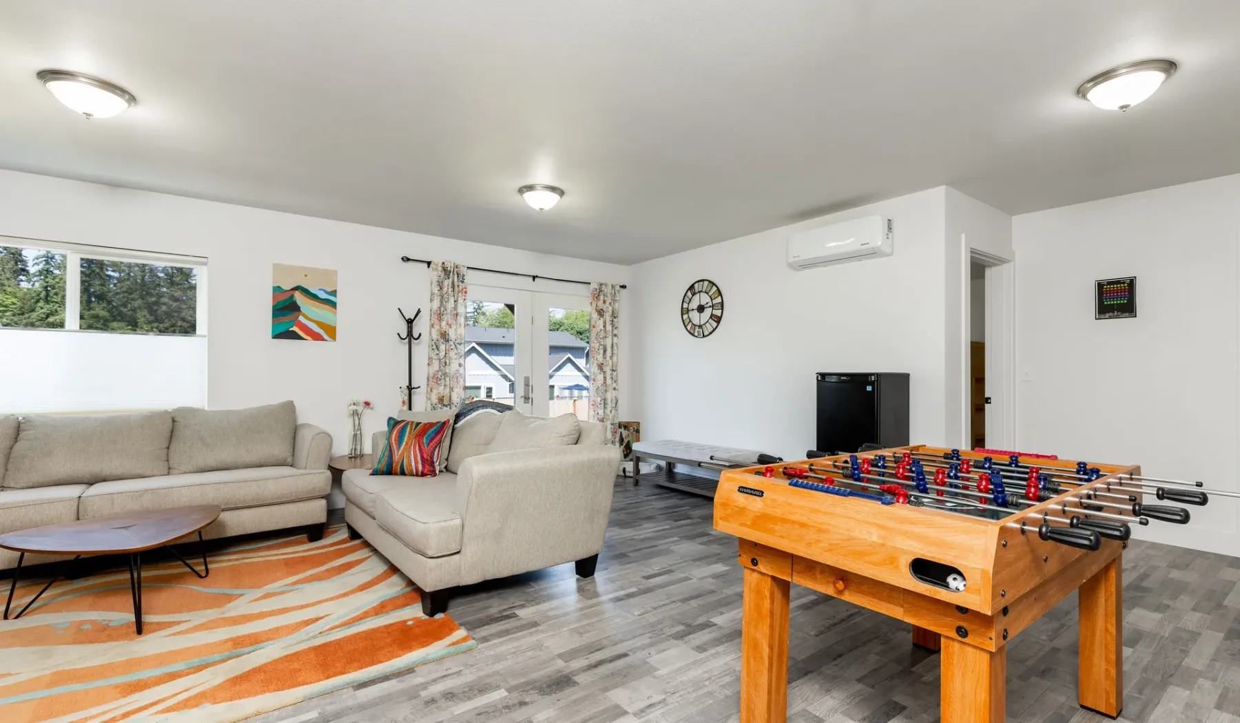 A bright living room with seating, windows, and a foosball table.