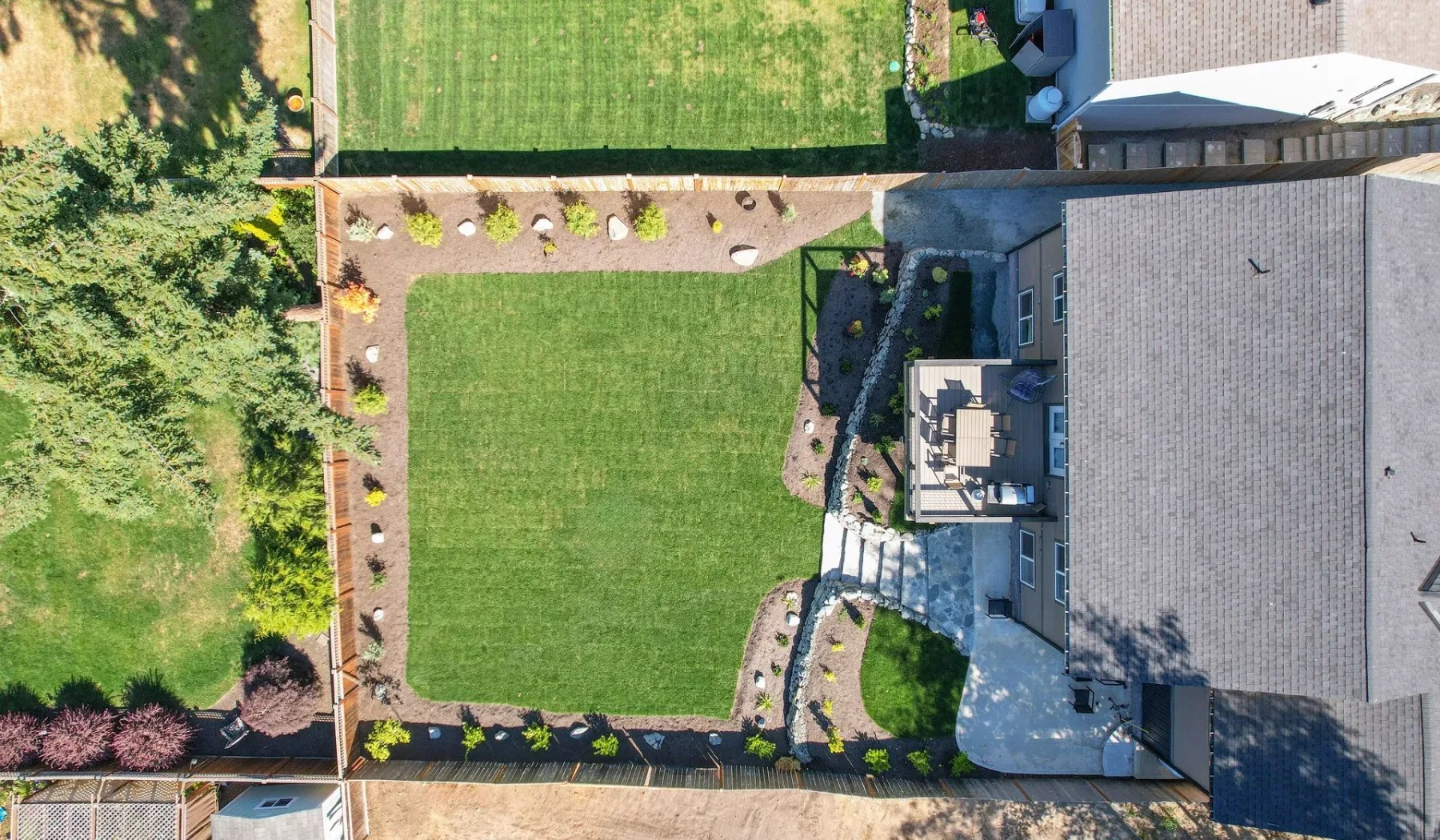Vista aérea de una casa junto a un césped rectangular y parterres ajardinados.