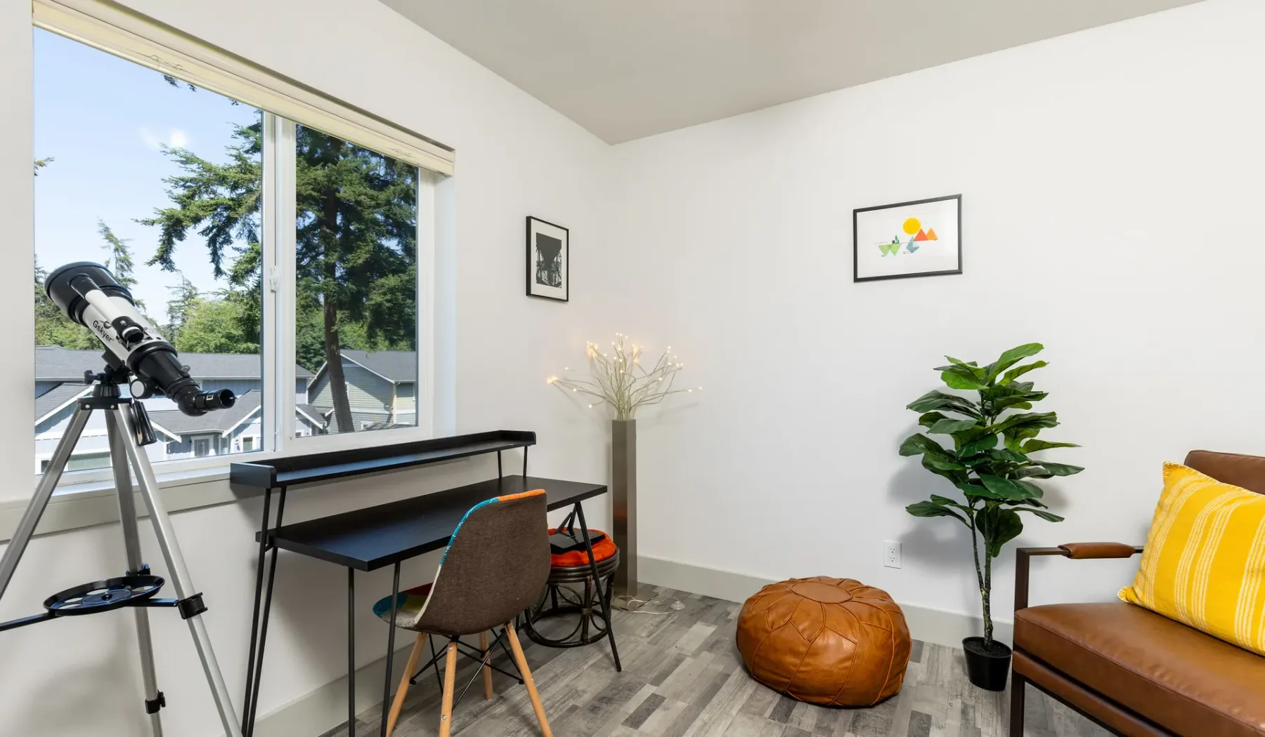 Una habitación luminosa con escritorio, telescopio y asientos junto a una ventana grande.