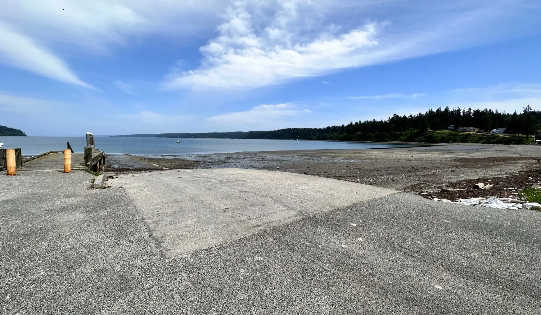 Una amplia zona pavimentada junto al agua llega a una orilla tranquila bajo un cielo parcialmente nublado.