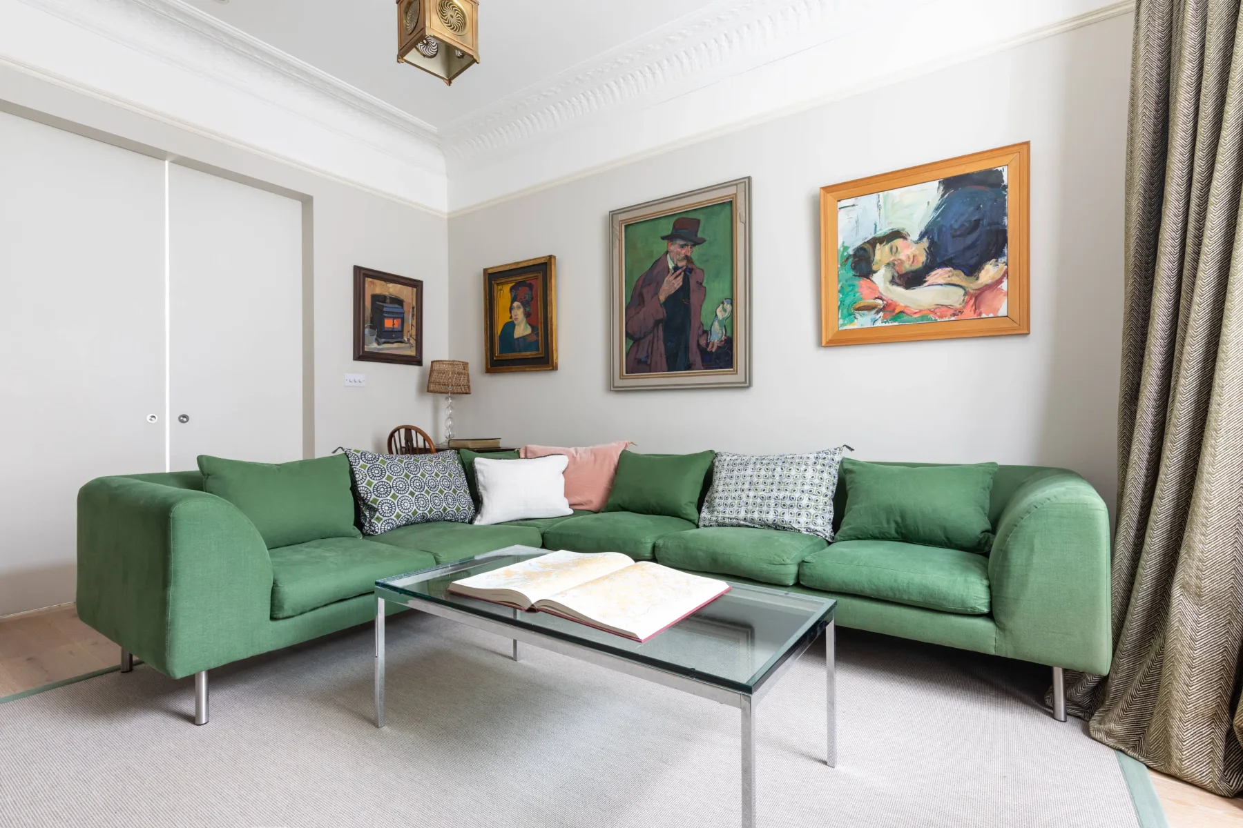 A living room with green seating, a glass coffee table, and framed artwork.