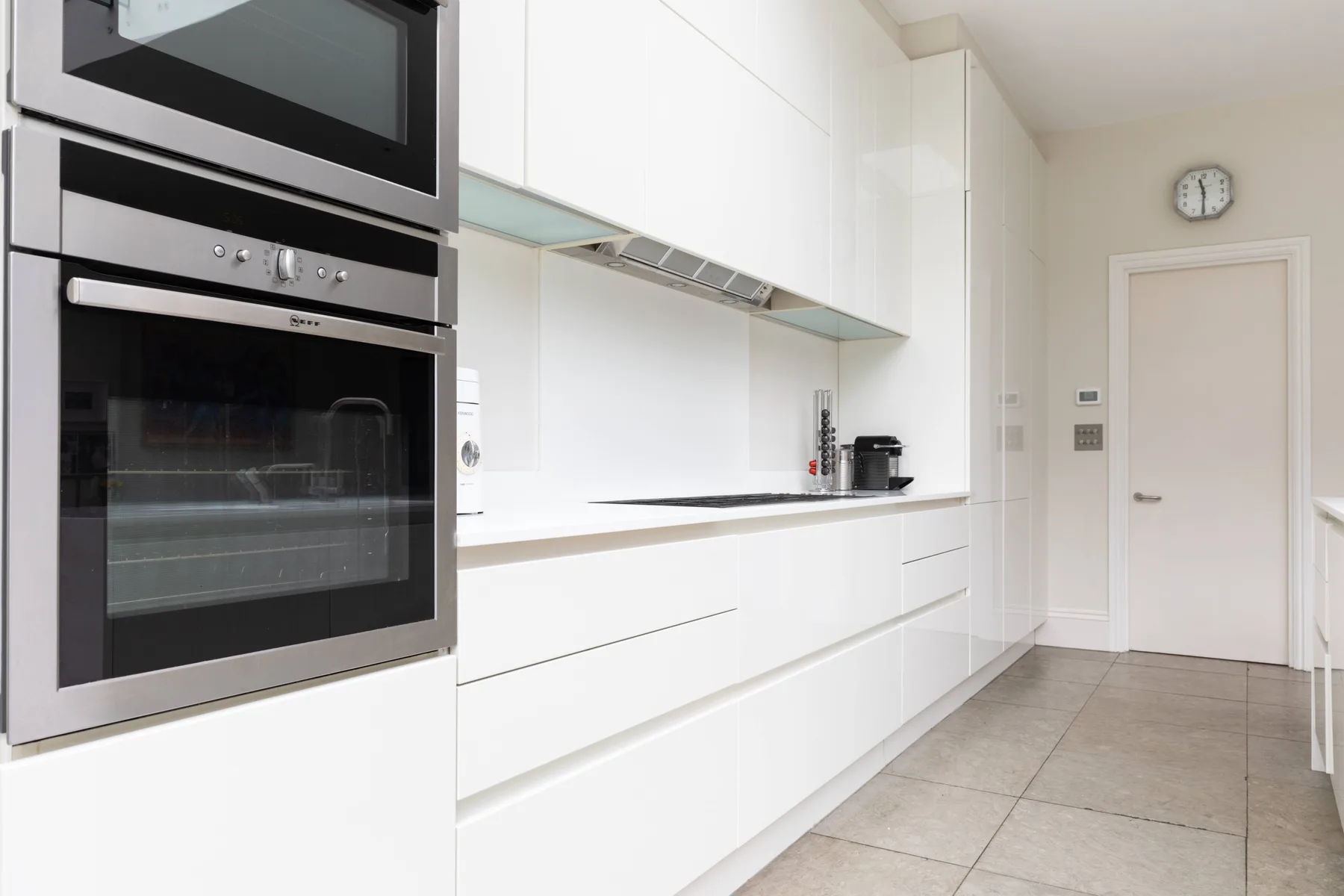 A bright modern kitchen with white cabinets and built-in ovens.