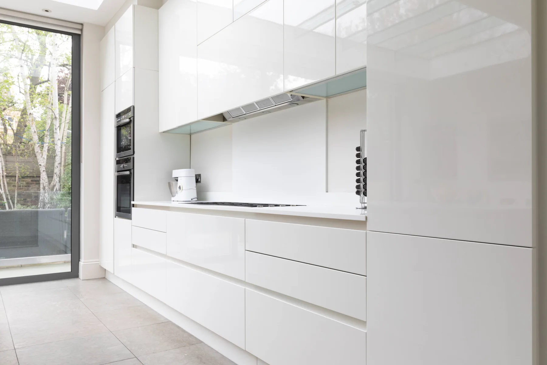 A bright modern kitchen with white cabinets and a large window.