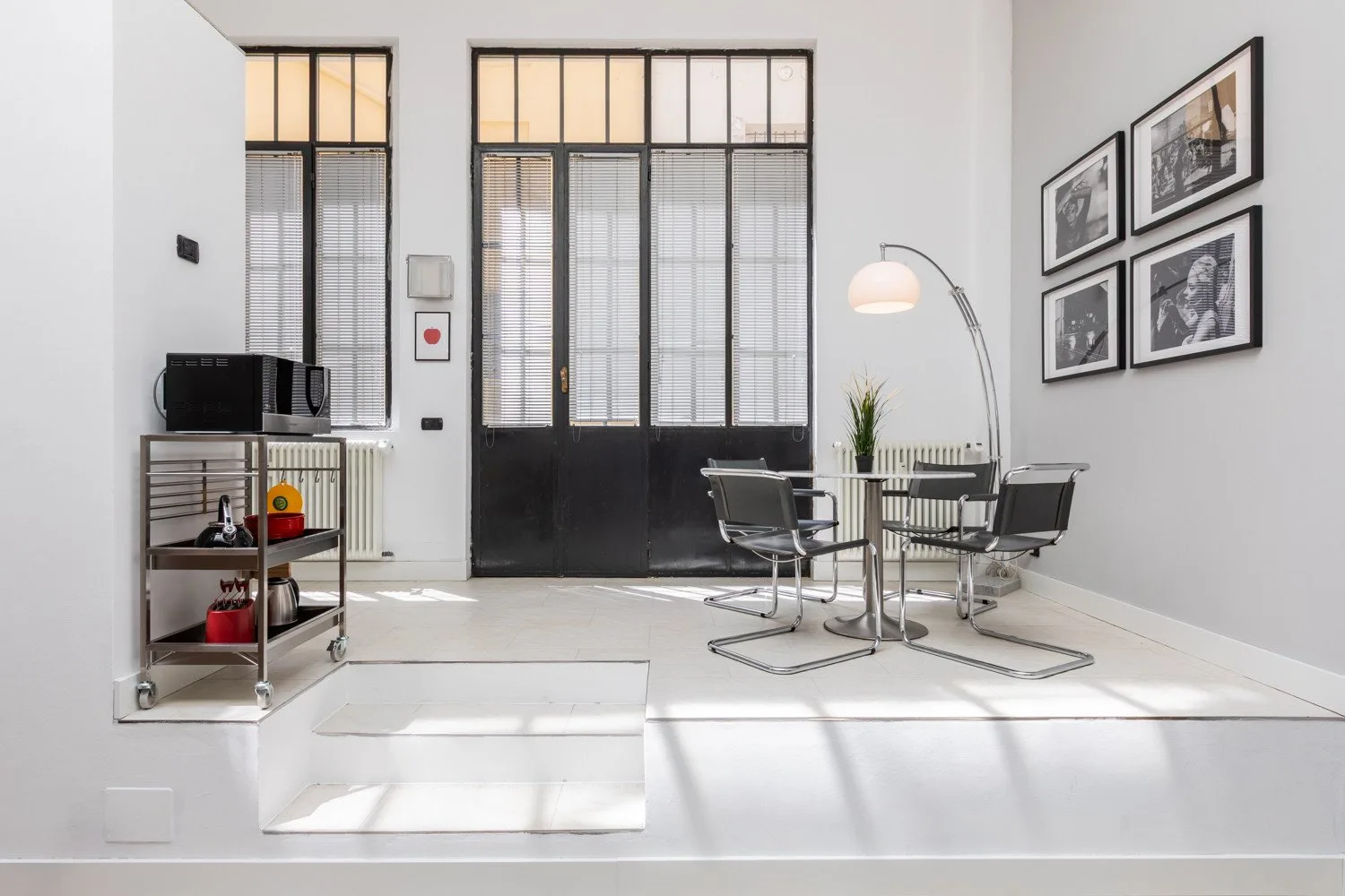 A bright dining area with a glass table, metal seating, and tall windows.