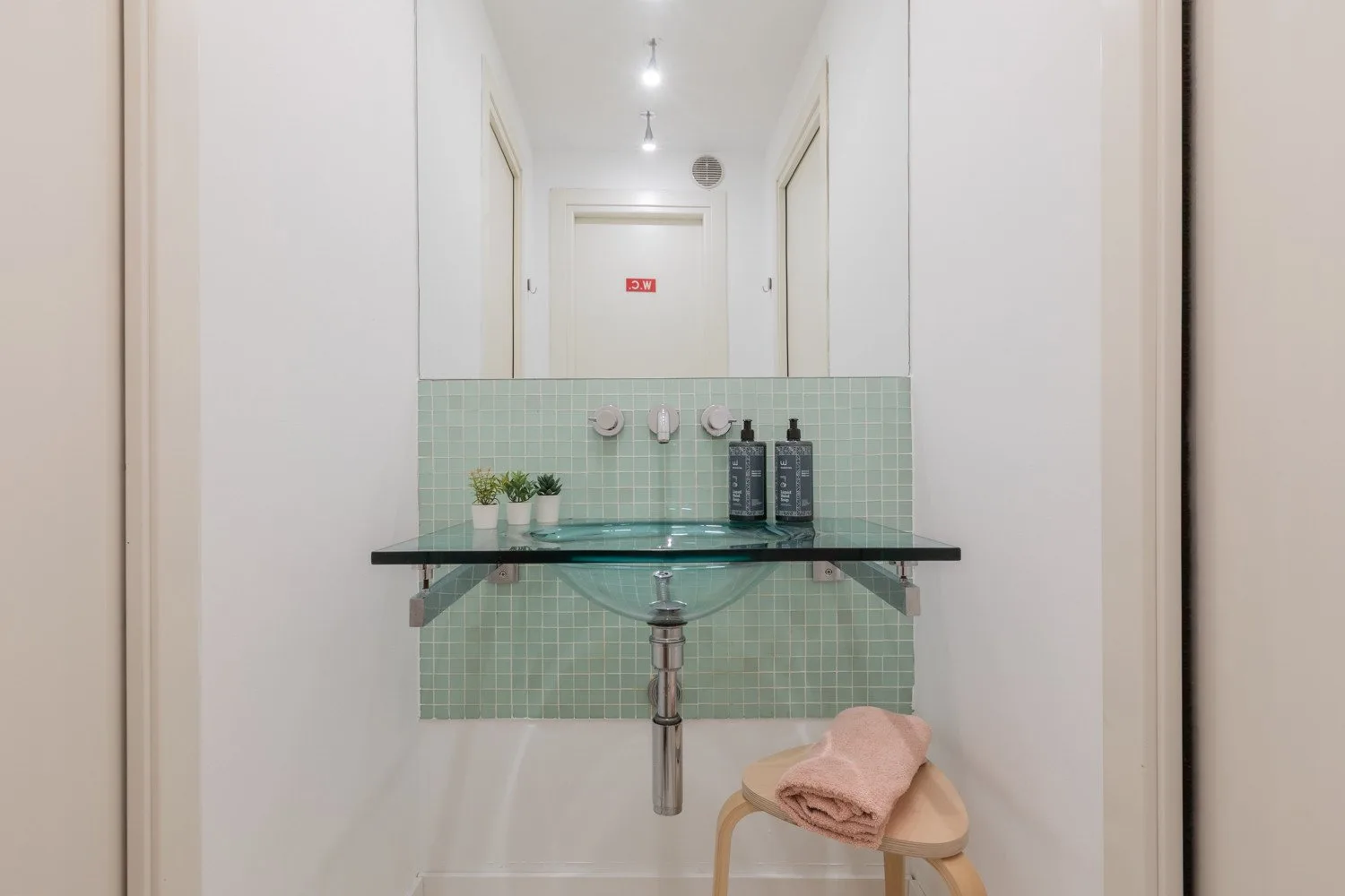 A bathroom vanity with a glass shelf, green tile, and a mirror.