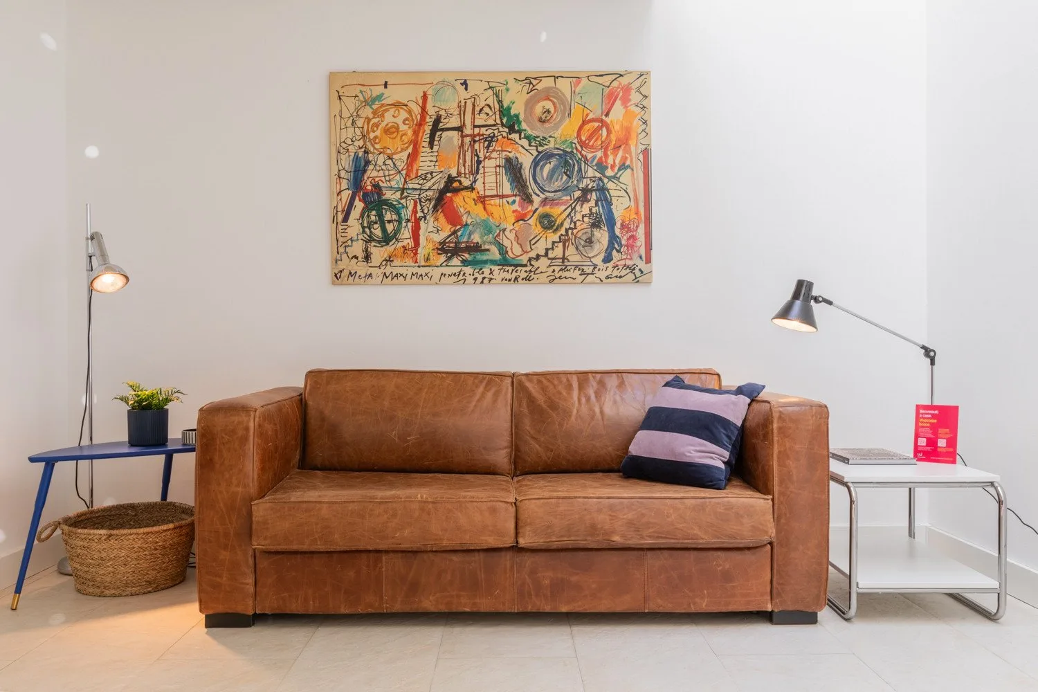 A living room with a brown sofa, colorful wall art, and side tables.