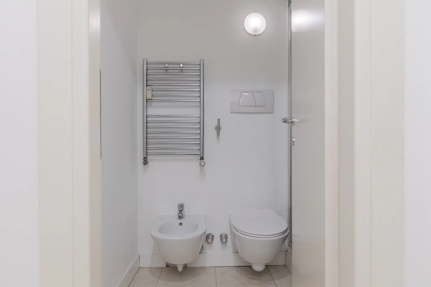 A bright bathroom with a bidet and toilet beneath a wall-mounted towel rack.
