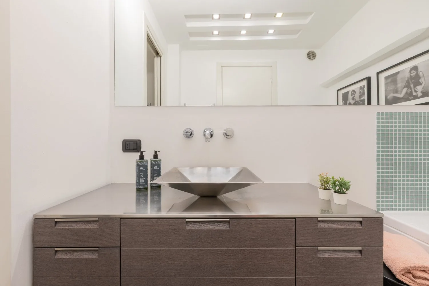 A modern bathroom vanity with a wide sink and framed artwork on the wall.