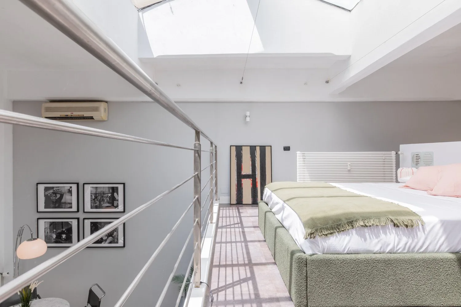 A bright loft bedroom with a bed beneath skylights and a metal railing.