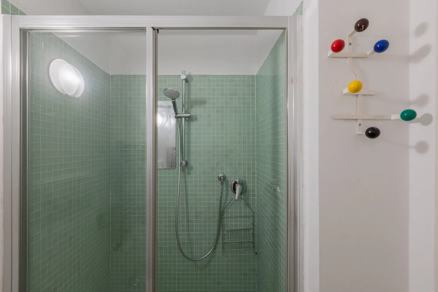A tiled shower area with a wall-mounted showerhead and handheld spray.