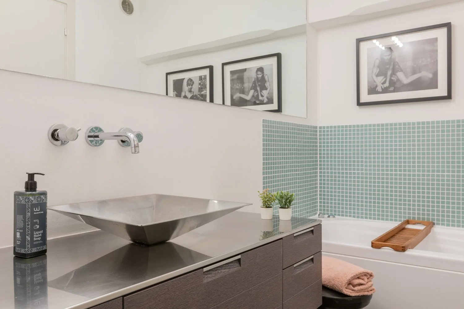 A modern bathroom with a vessel sink, bathtub, and green tiled wall.