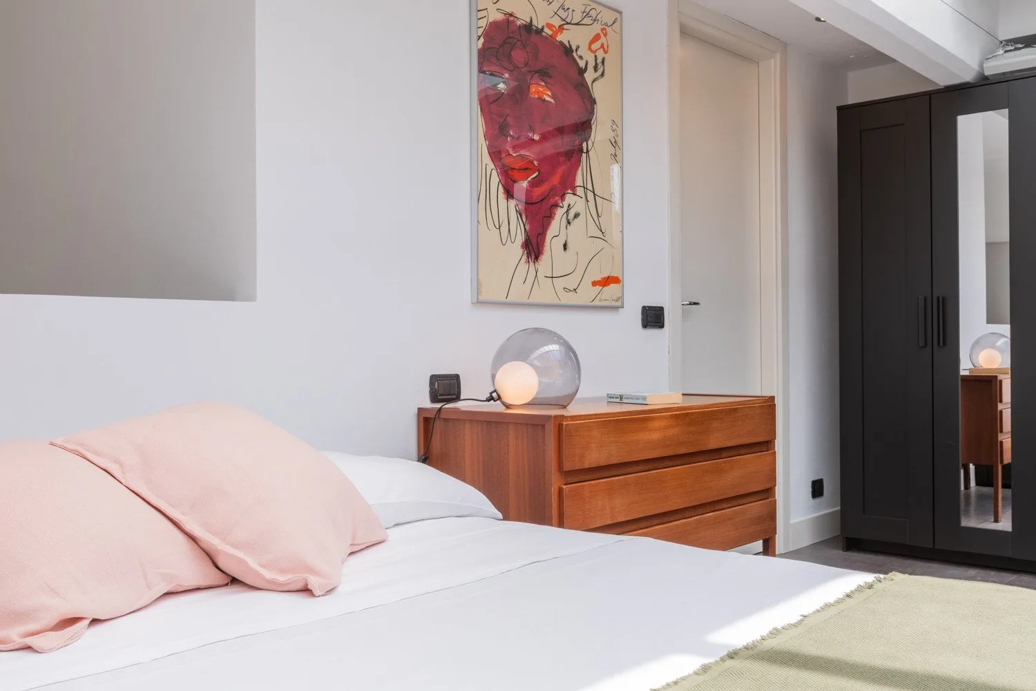 A bedroom with a bed, wooden dresser, and colorful portrait artwork.