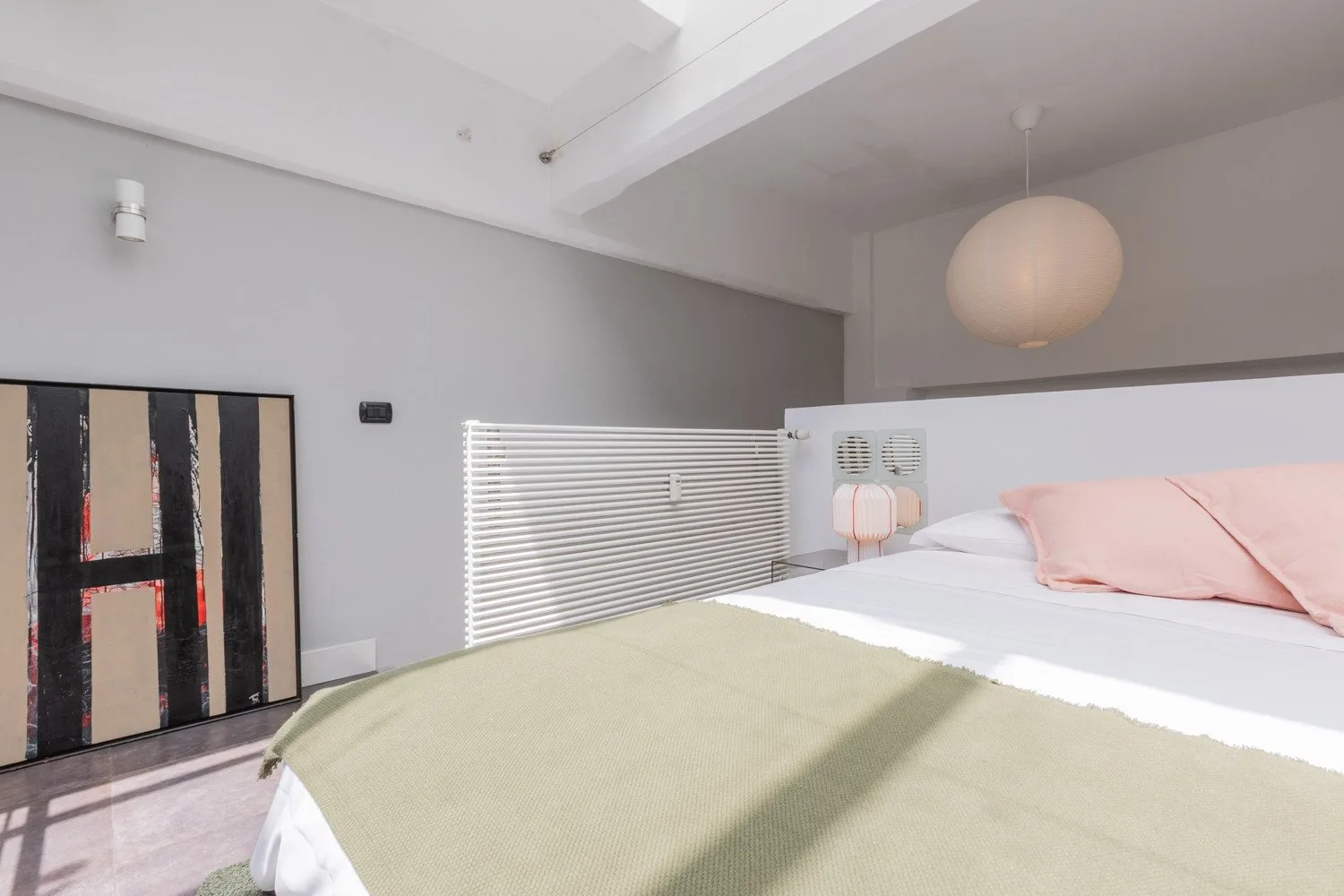 A bedroom with a bed covered by a pale green blanket and pink pillows.