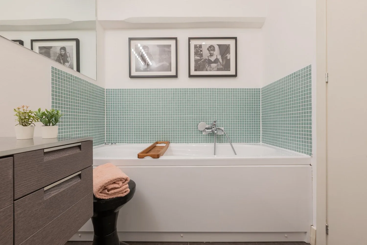 A bathroom with a bathtub, green tiled walls, and framed pictures above.