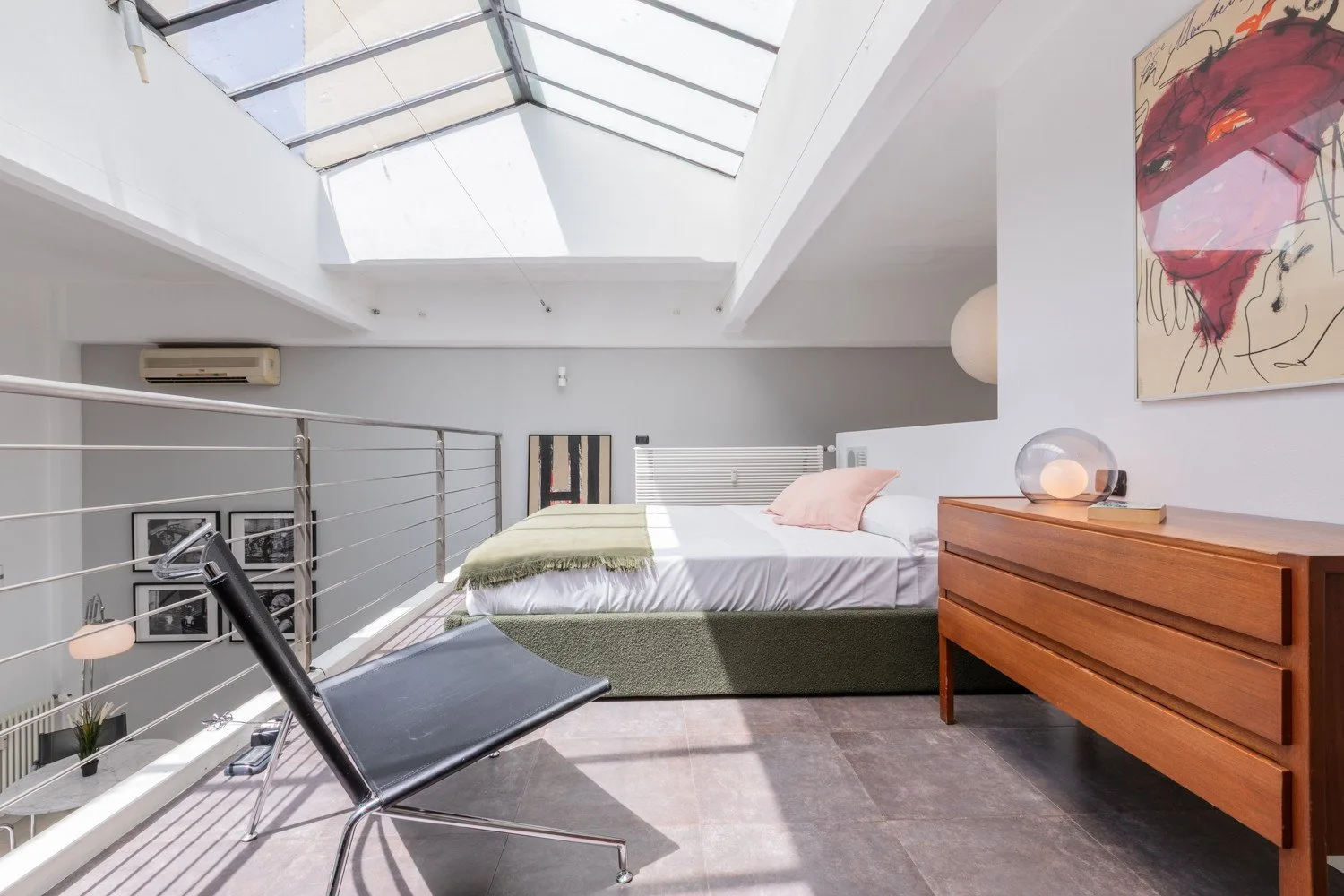A bedroom with a bed beneath a large skylight and a wooden dresser.