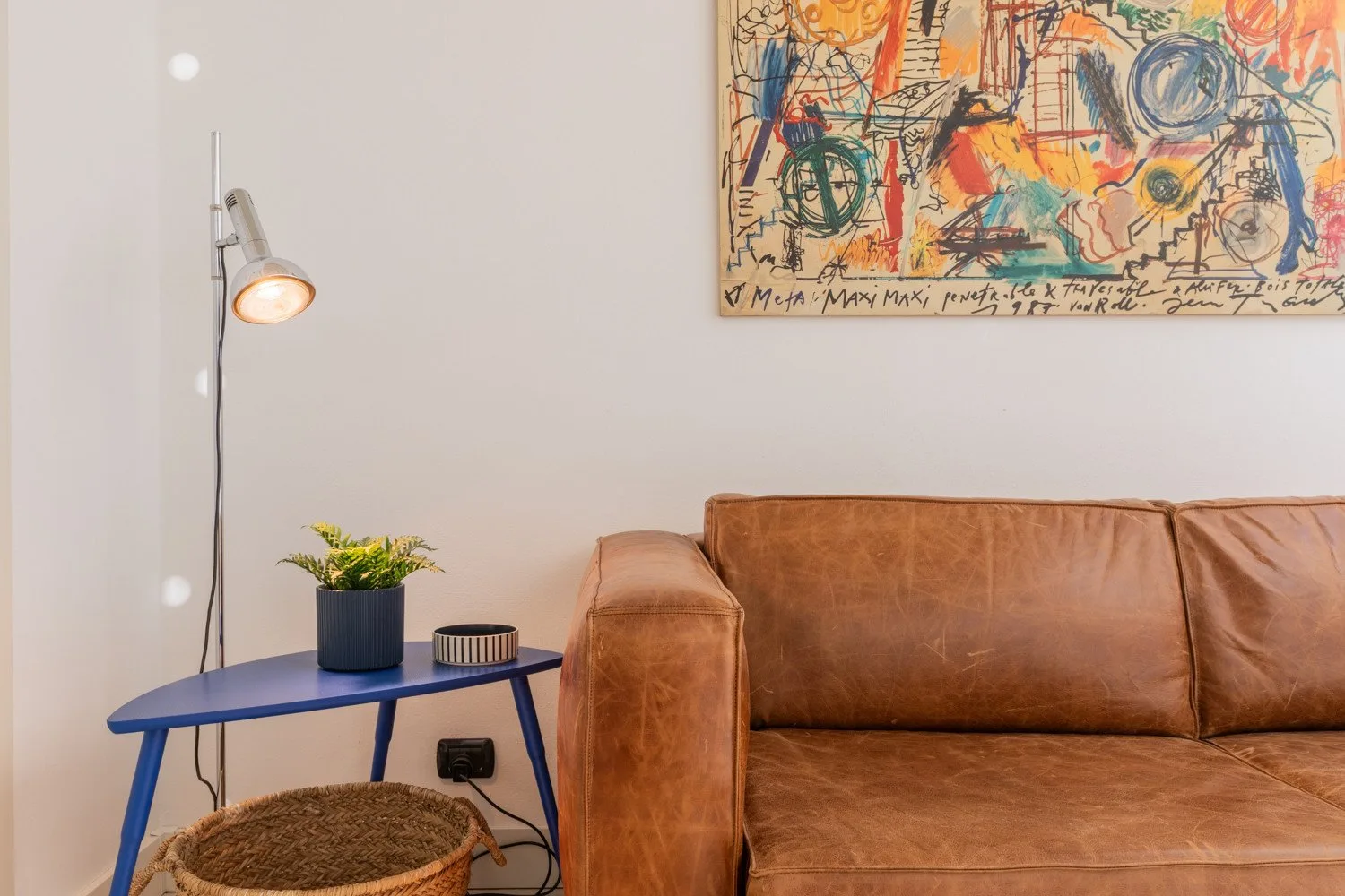A living room with a brown sofa, blue side table, and colorful wall art.