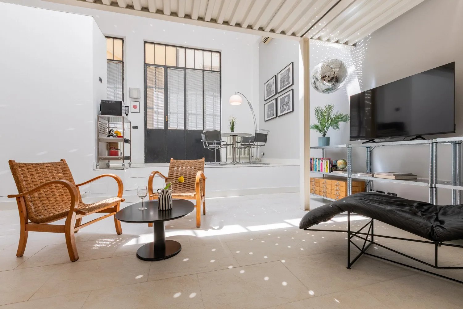 A bright living room with seating, a television, and a dining area by tall windows.
