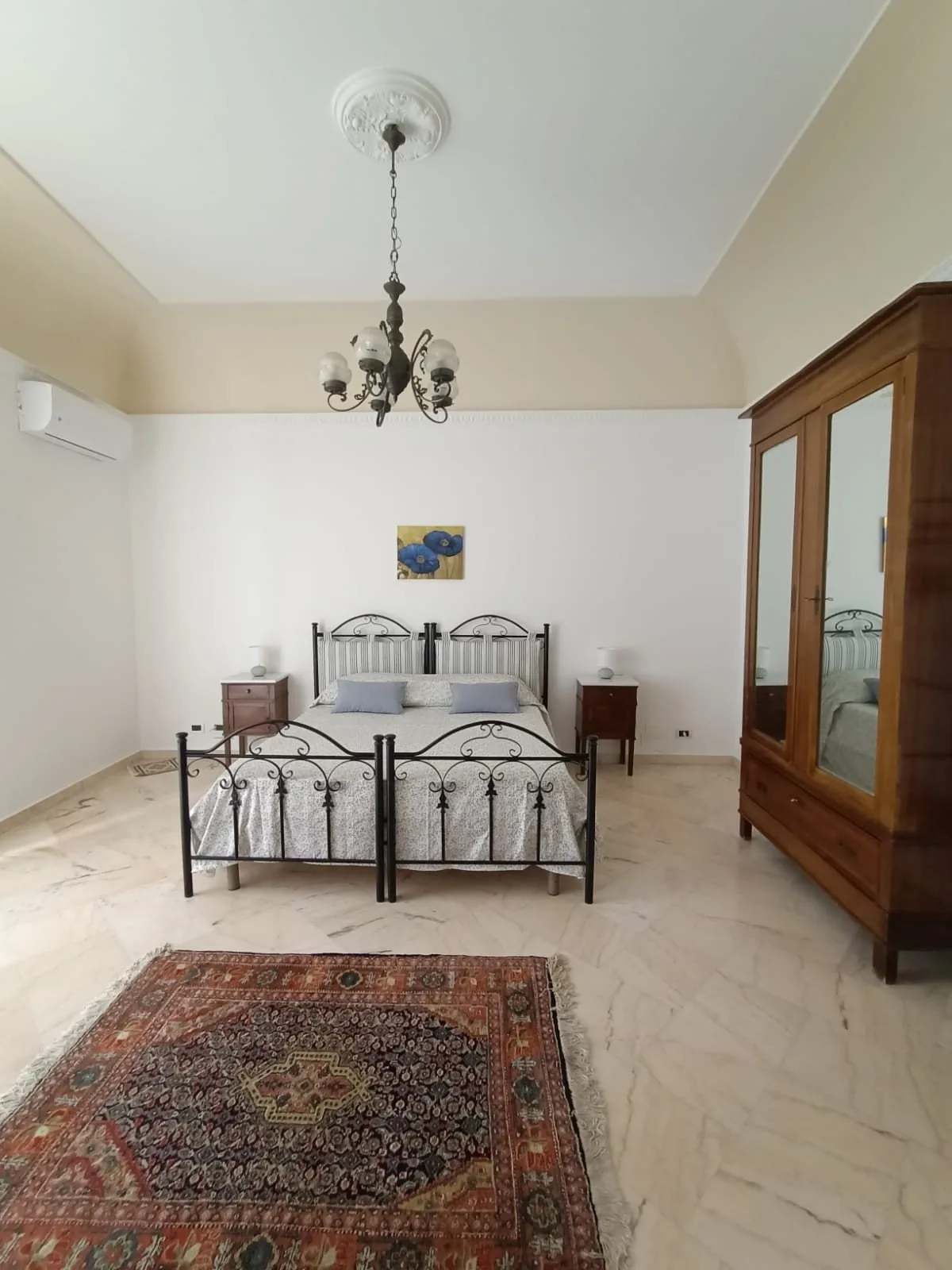 A bedroom with a metal bed, bedside tables, and a patterned rug.