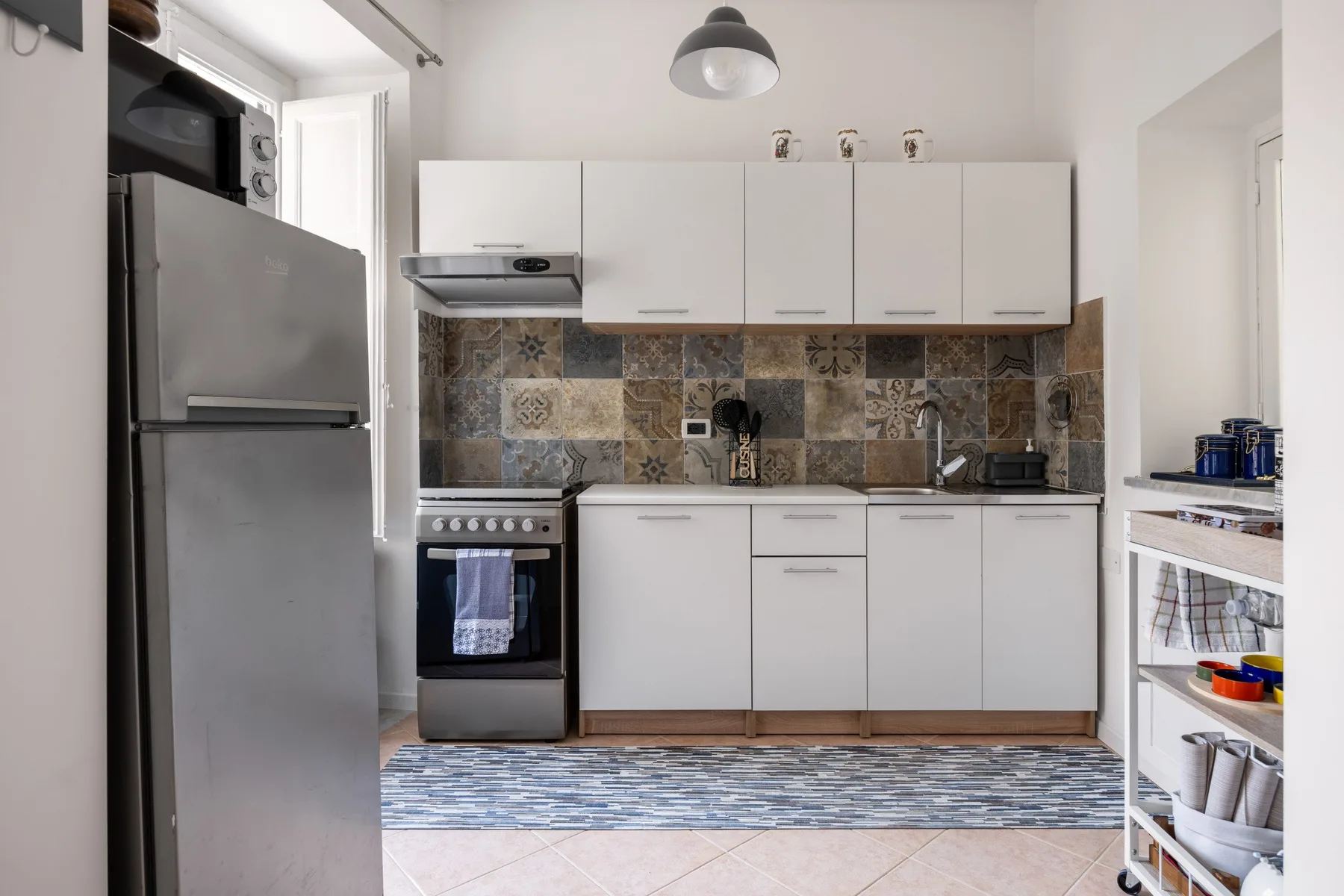 A bright kitchen with white cabinets, stainless steel appliances, and a patterned backsplash.