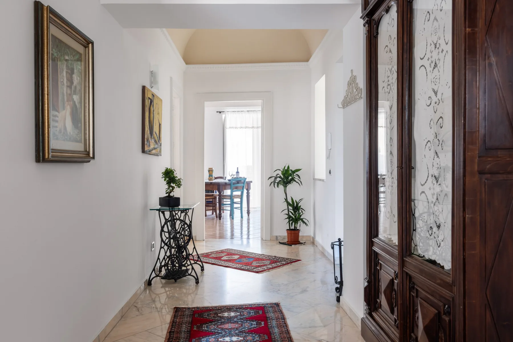 A bright hallway leads to a dining area, with framed art and rugs along the way.