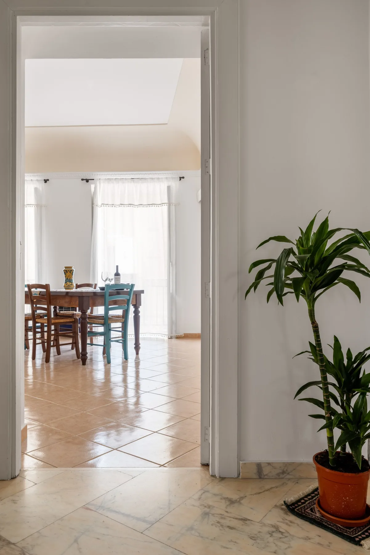 A dining area with a wooden table and chairs sits beyond a tiled doorway.