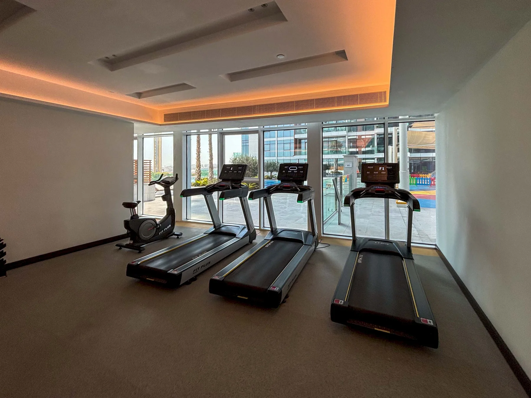 Una sala de ejercicio con cintas de correr y una bicicleta estática junto a ventanales.