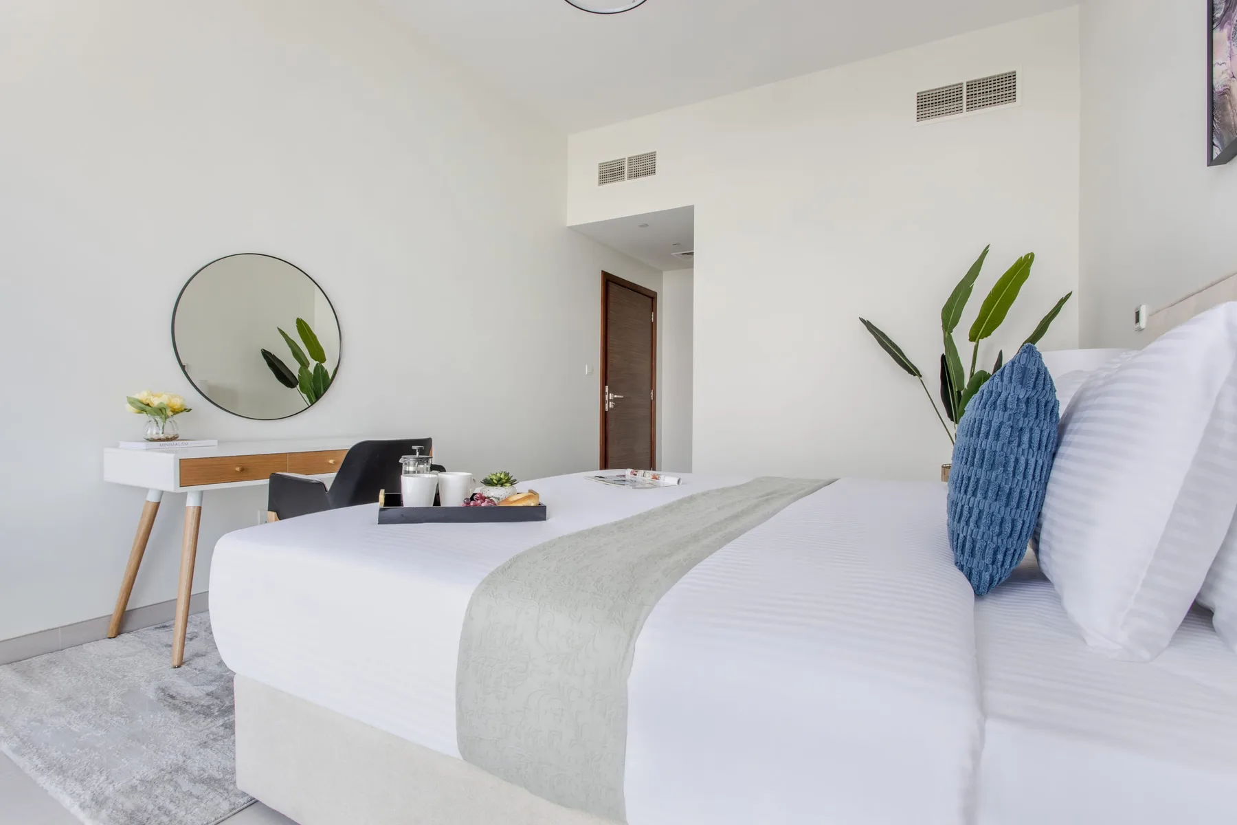 Un dormitorio luminoso con una cama tendida y un pequeño escritorio al lado.